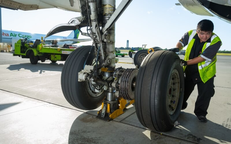An Aloha Tech Ops employee under the plane working on a plane tire.