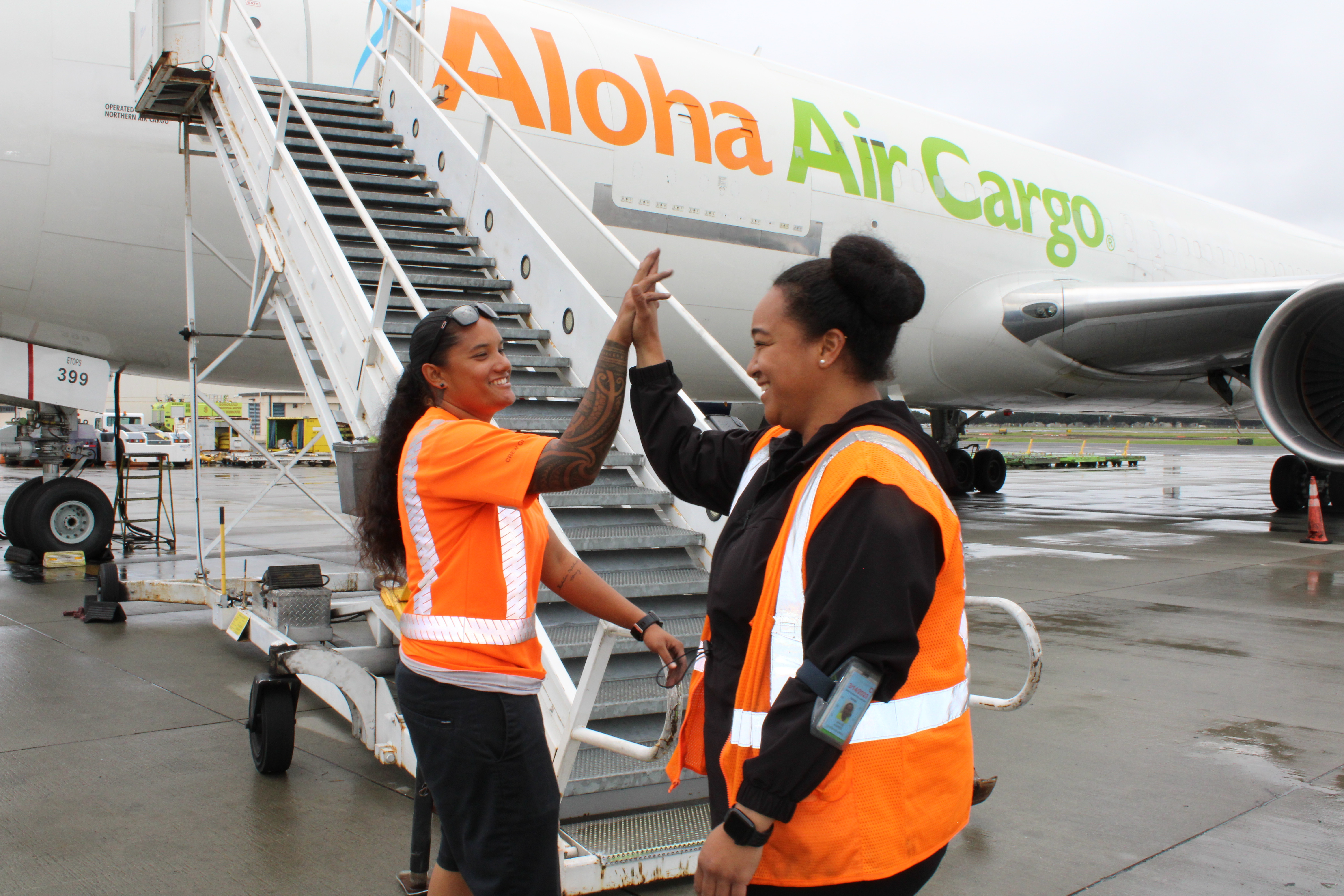 Two Aloha Air Cargo employees high fiving in front of a plane.