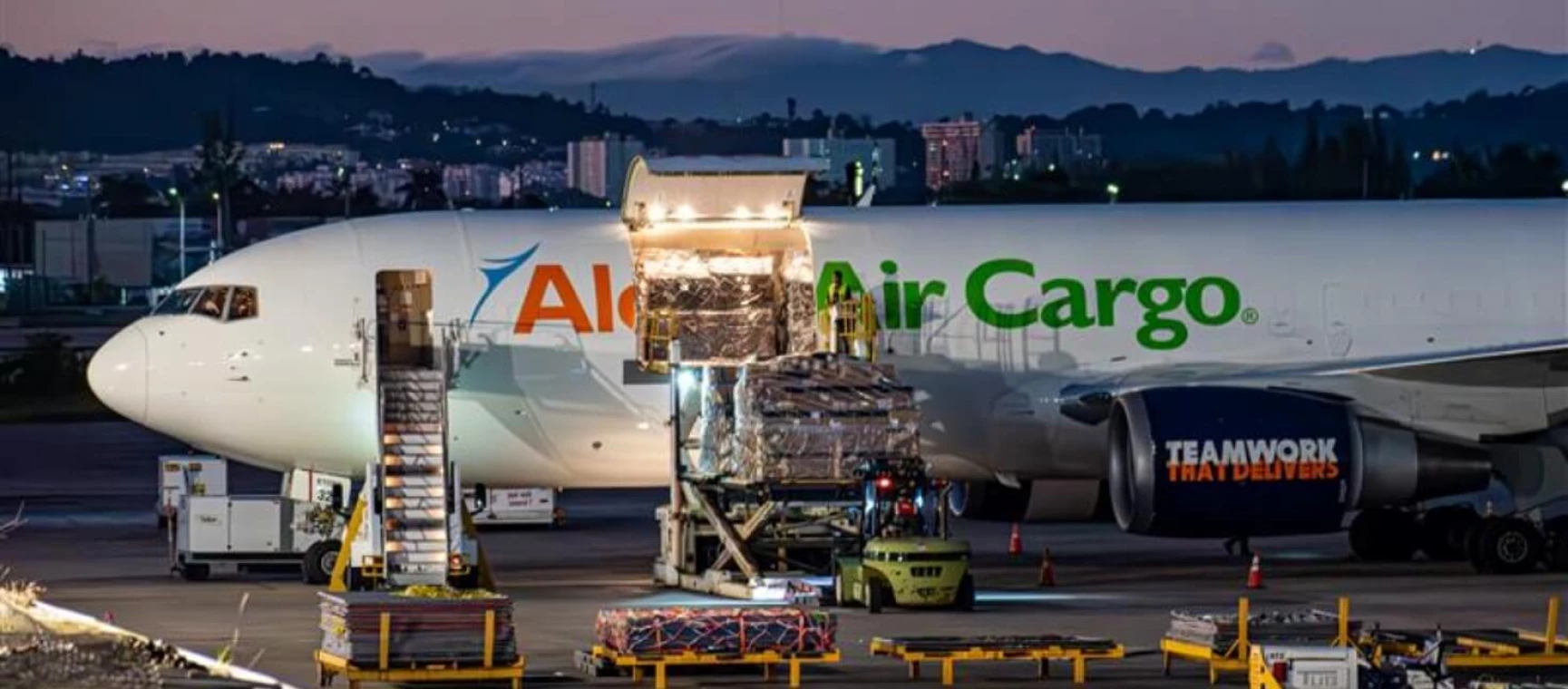 A wide angle shot of an Aloha Air Cargo plane while employees are loading cargo into it.