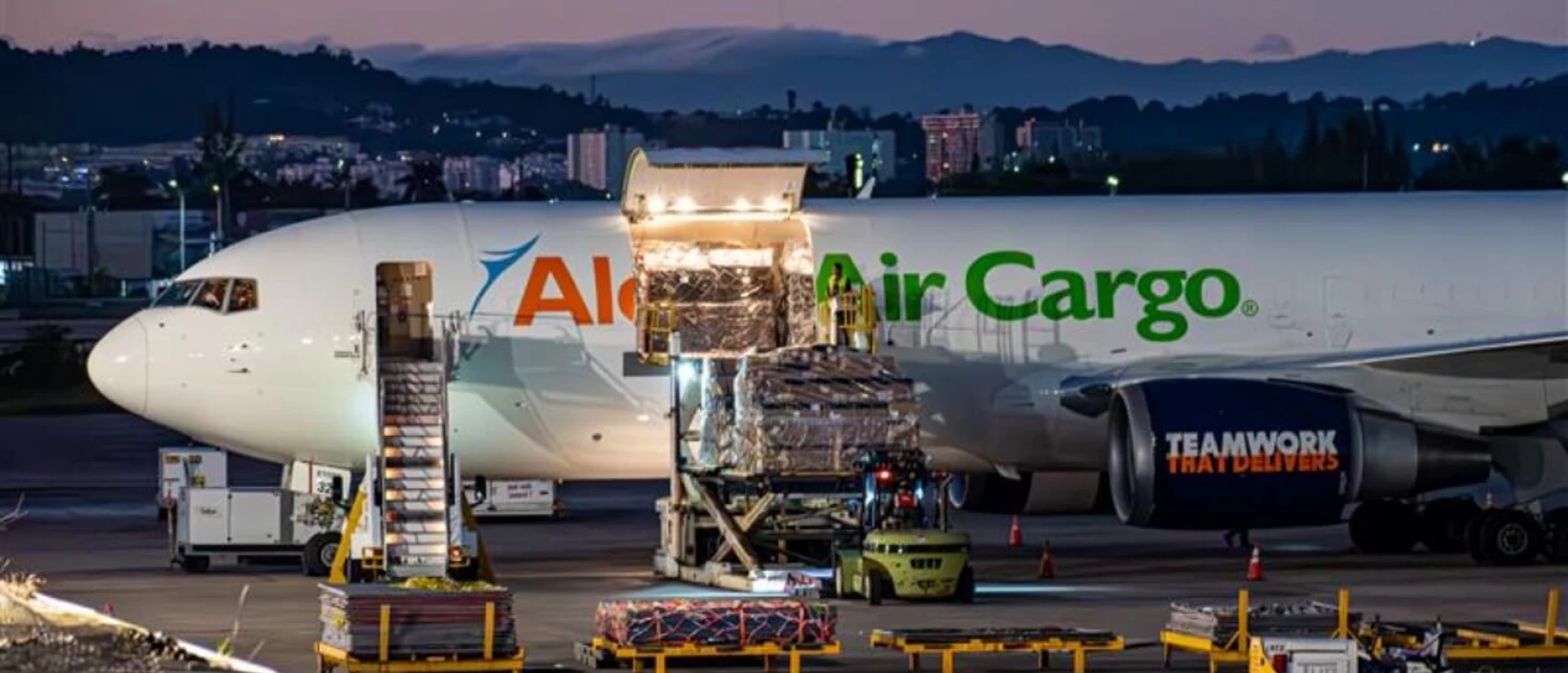 A wide angle shot of an Aloha Air Cargo plane while employees are loading cargo into it.