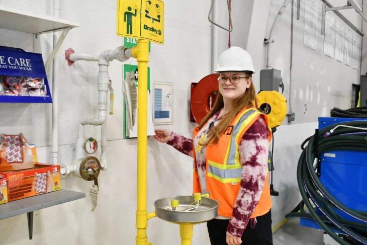 A NAMS employee wearing a hard hat and safety vest while standing in front of the safety wash area.