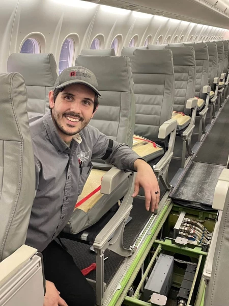 A NAMS employee sitting in a seat on a passenger plane and smiling for the camera.
