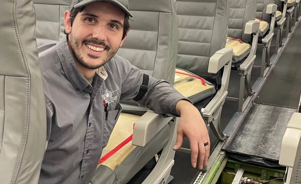 A NAMS employee sitting in a seat on a passenger plane and smiling for the camera.