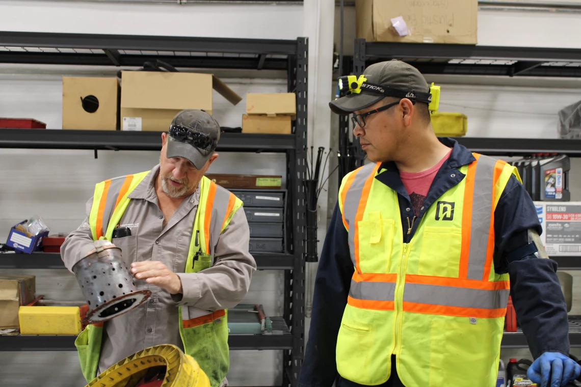 Two NAMS mechanics talking while looking at a part for a plane.