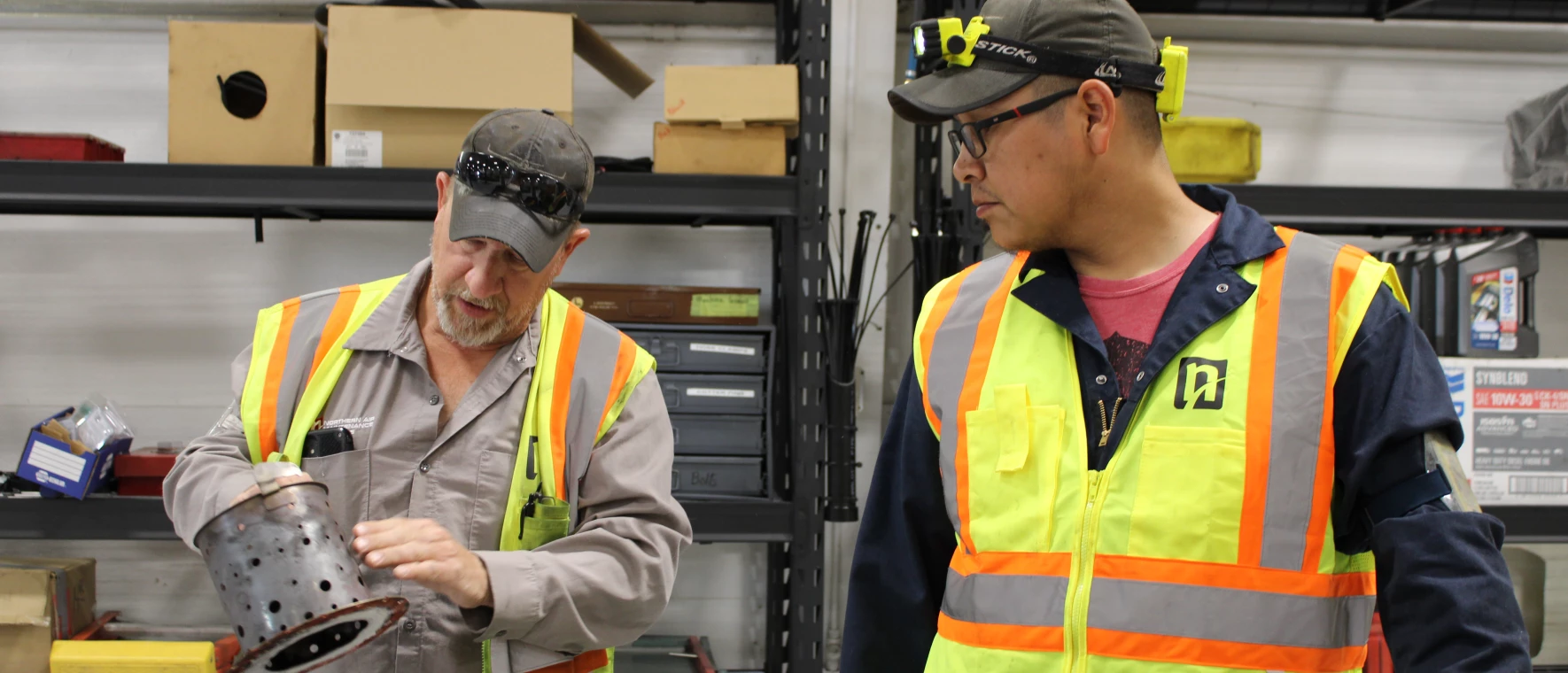 Two NAMS mechanics talking while looking at a part for a plane.