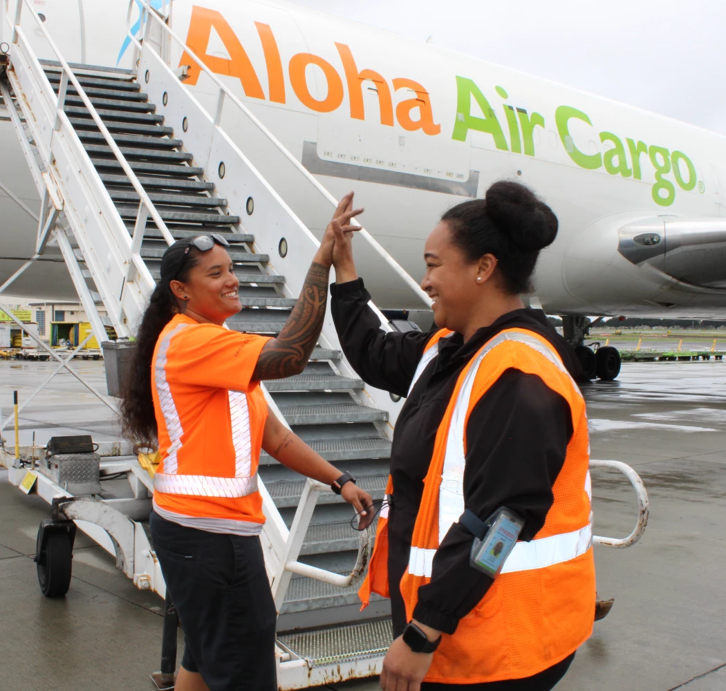 Two Aloha Air Cargo employees high fiving in front of a plane.
